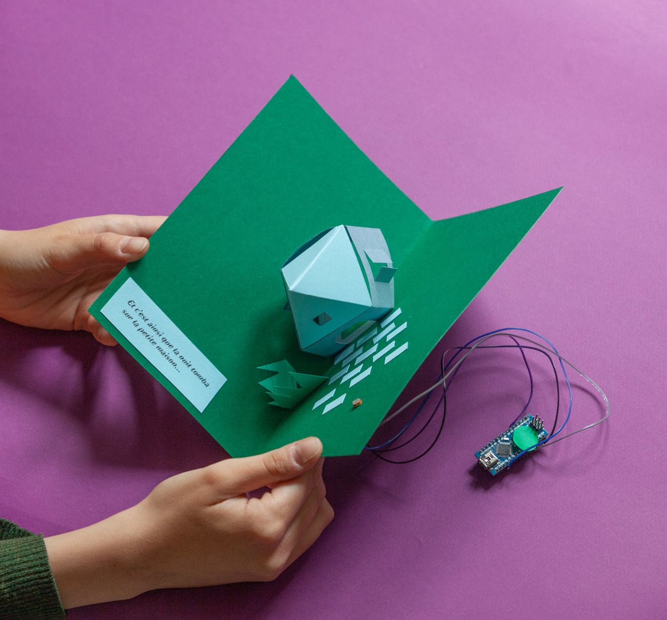 Carte pop-up en papier vert avec une maison de papier et un circuit électronique, sur fond violet